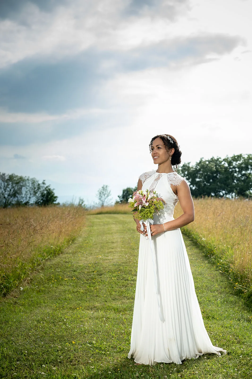 Bride holding her bouquet in a green meadow under an open sky
