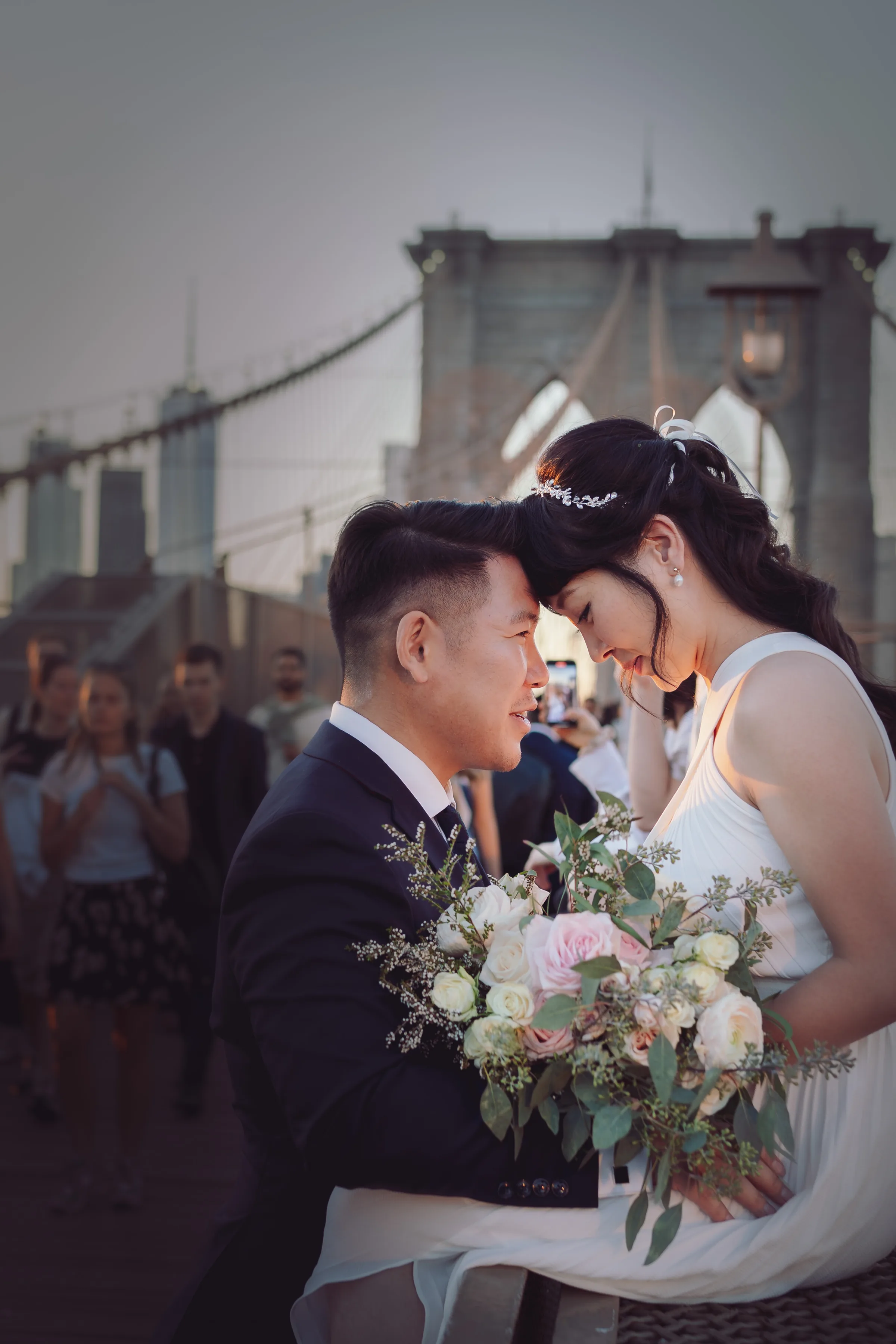 Bride and groom touching foreheads with a city bridge behind them