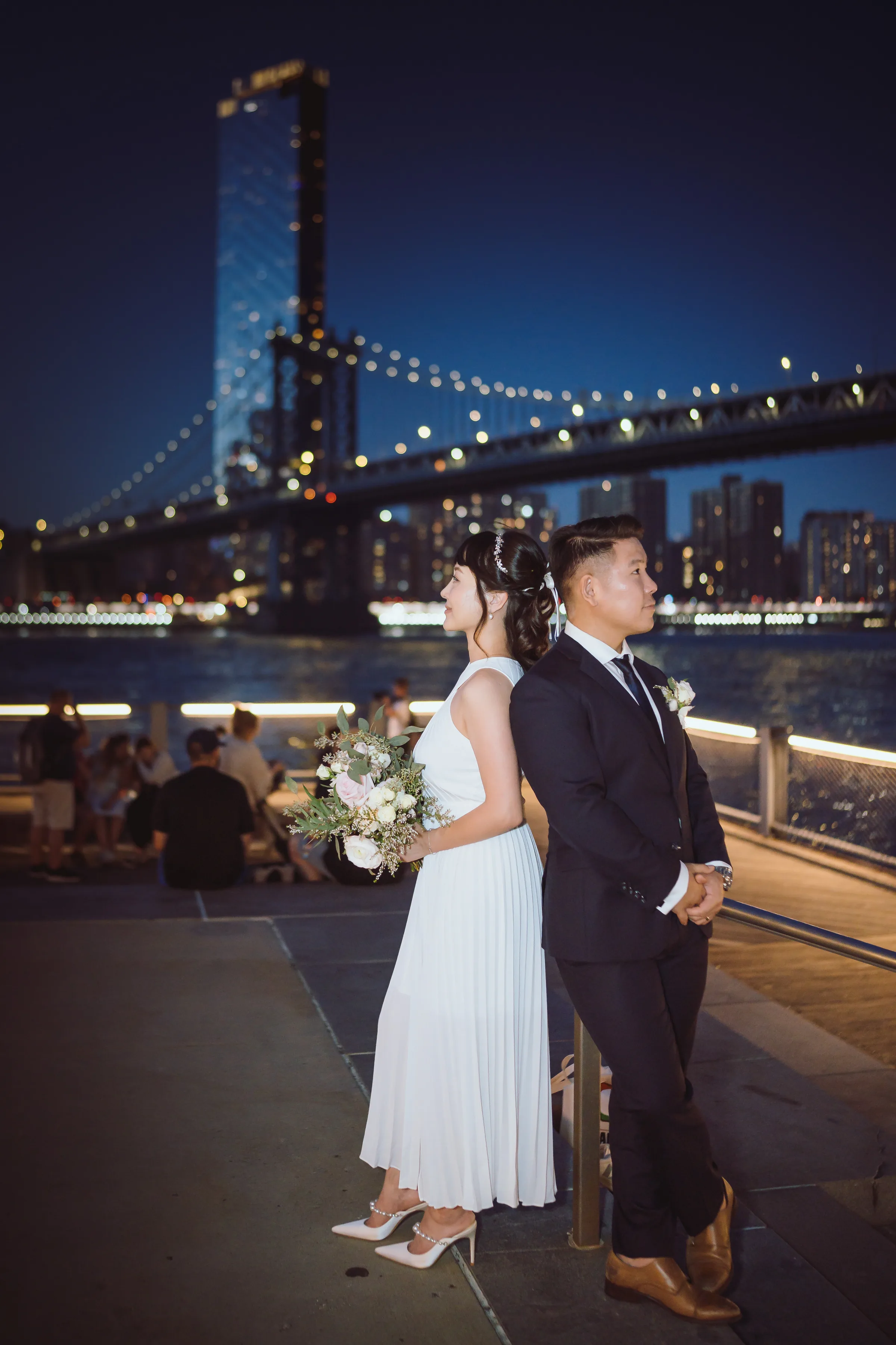 Bride and groom overlooking the river and an illuminated city bridge at night