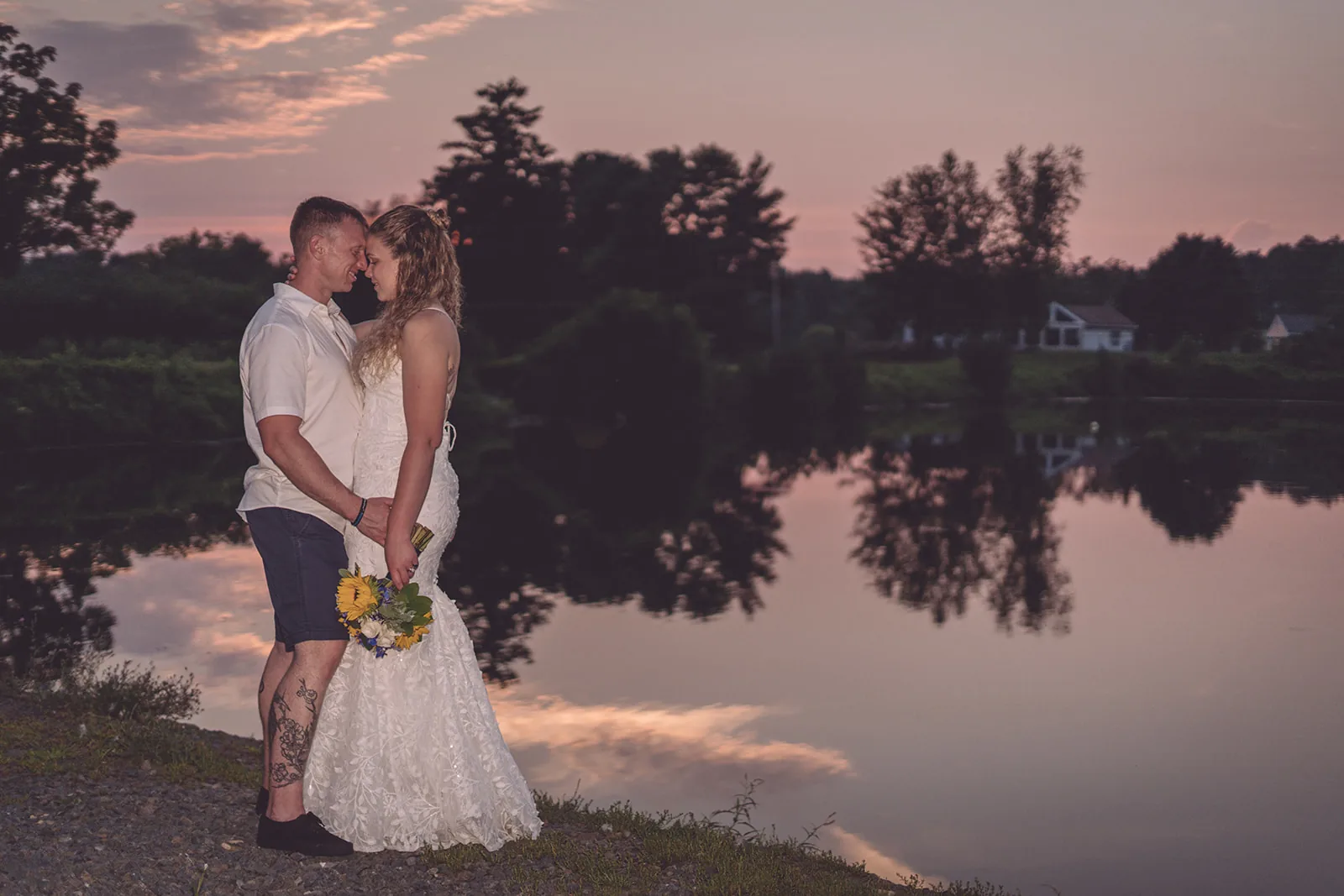 Couple kissing beside still water under a pink evening sky