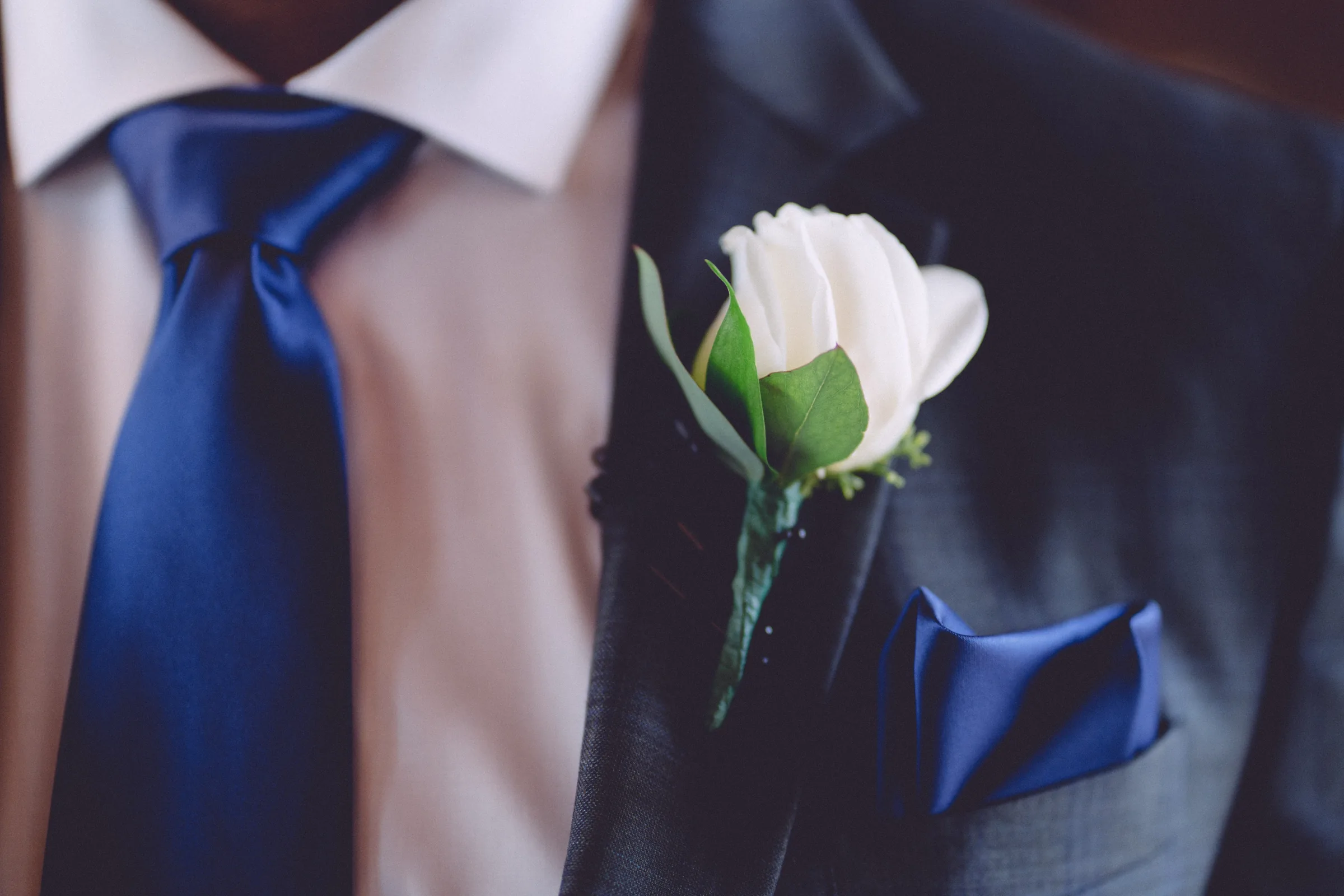 White rose boutonniere and blue tie on the groom's wedding suit