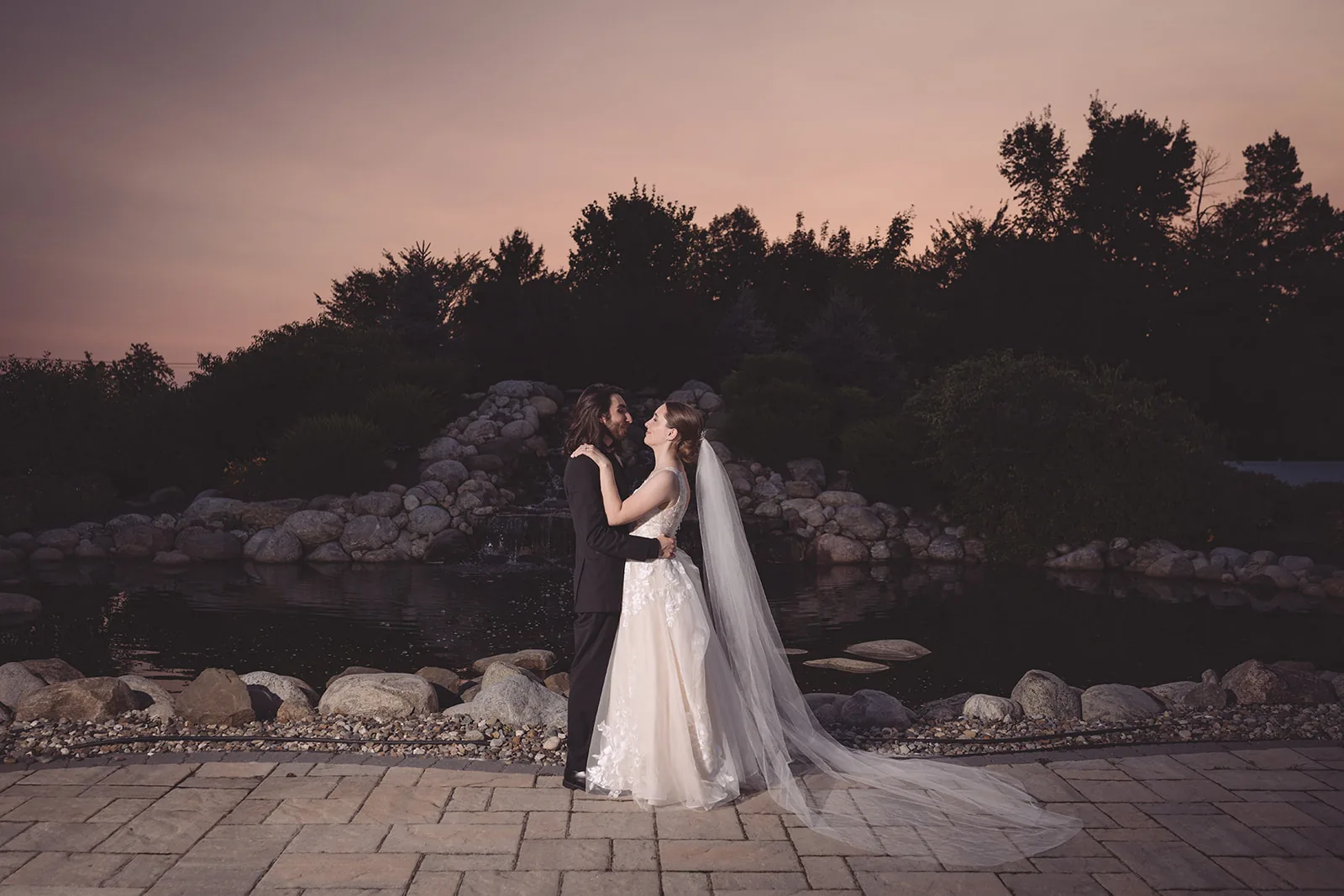 Couple embracing on a rocky shoreline beneath a pastel sunset