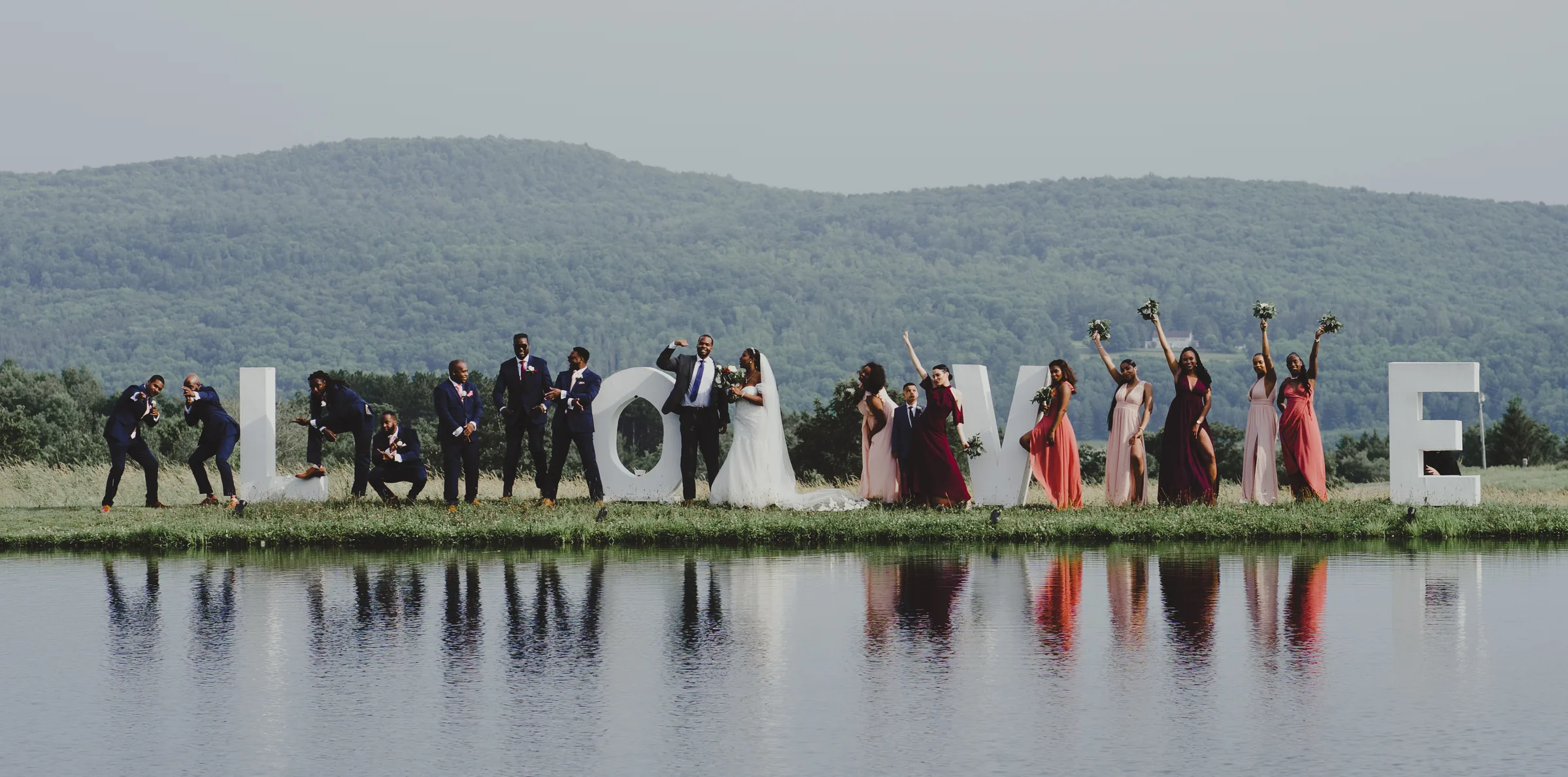 Wedding party reflected in a still pond with mountains in the distance