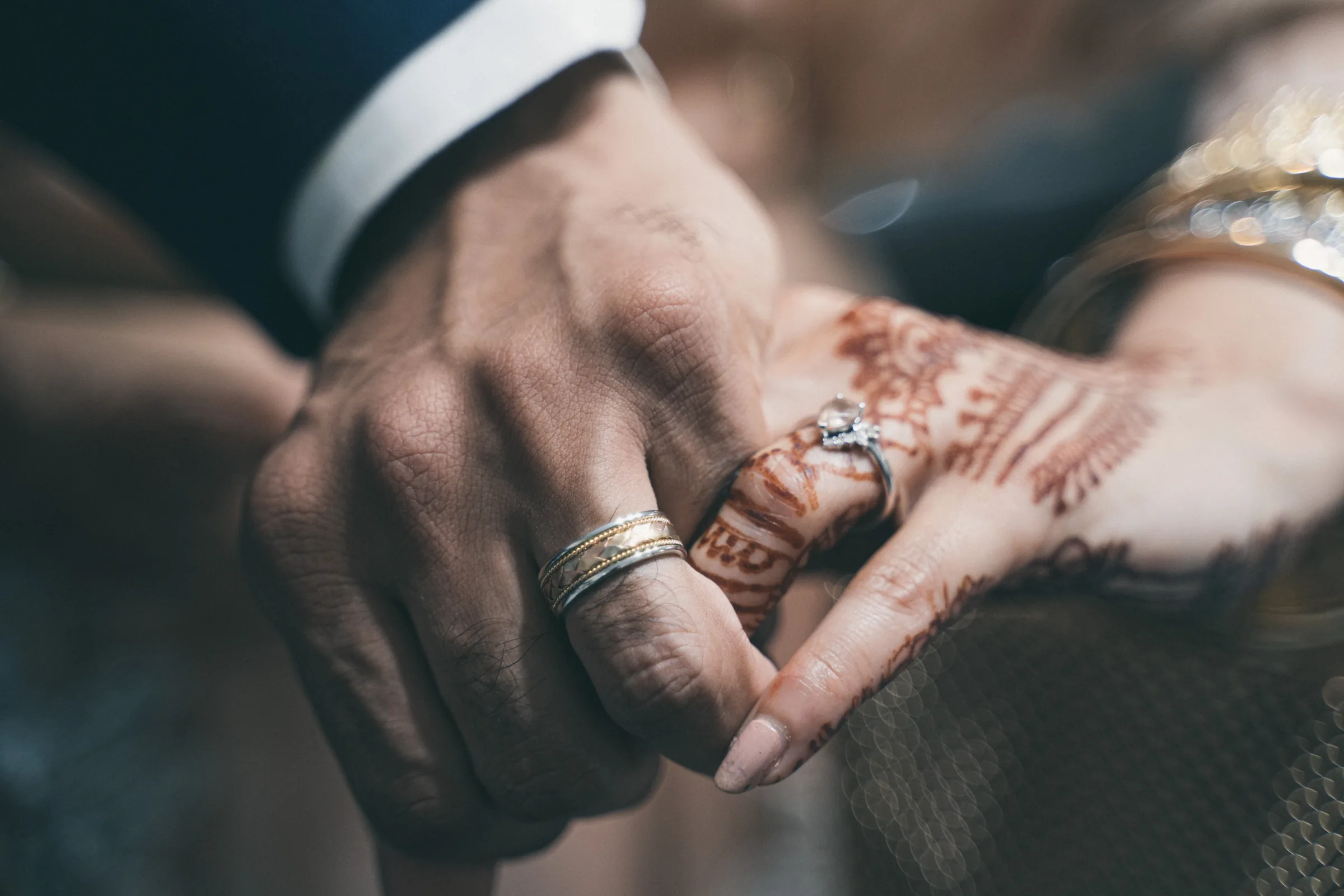 Close view of a couple's hands showing wedding rings and henna