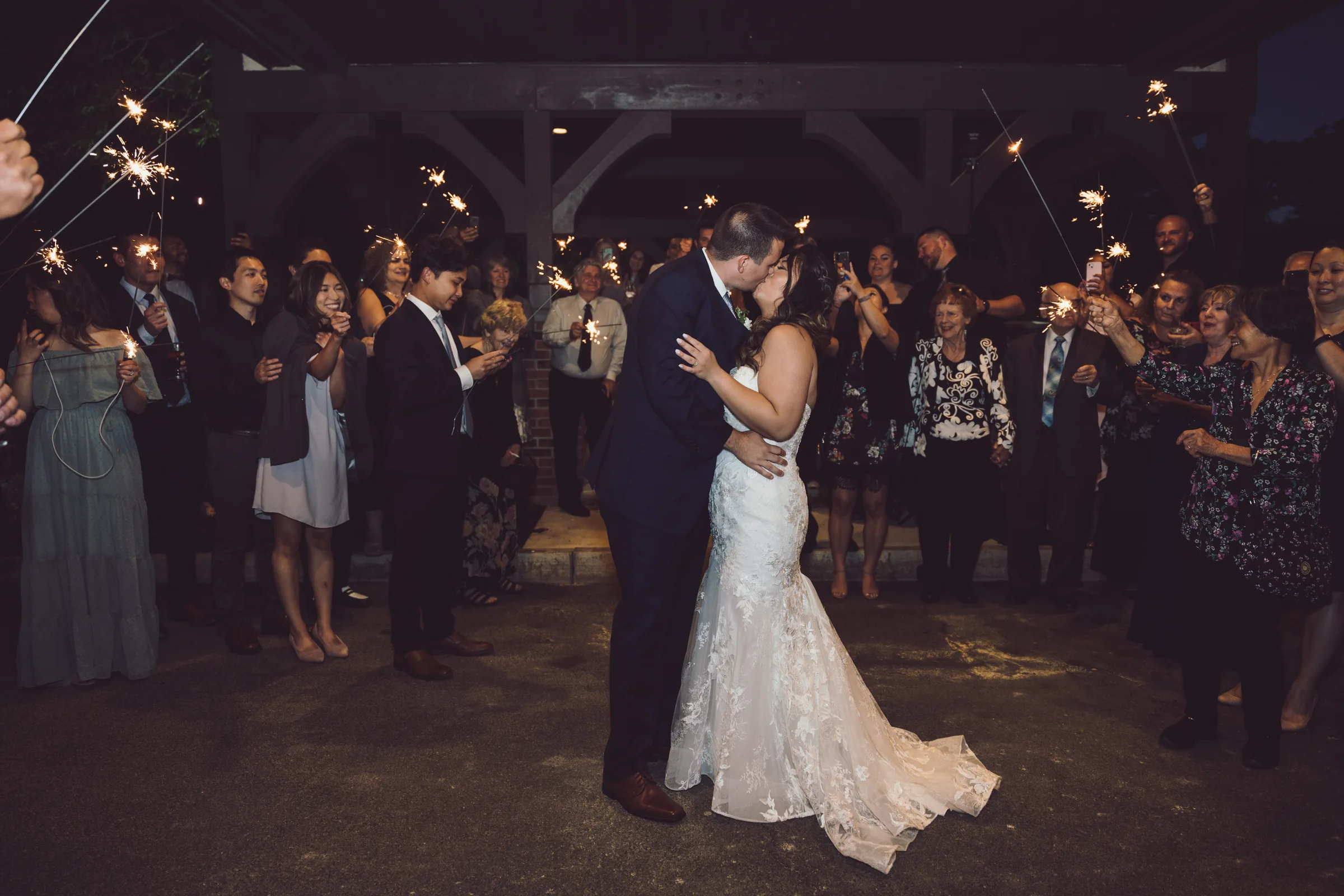 Bride and groom kissing as wedding guests surround them with sparklers