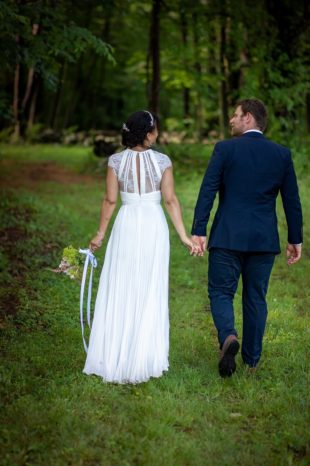 Bride and groom walking hand in hand along a green woodland path